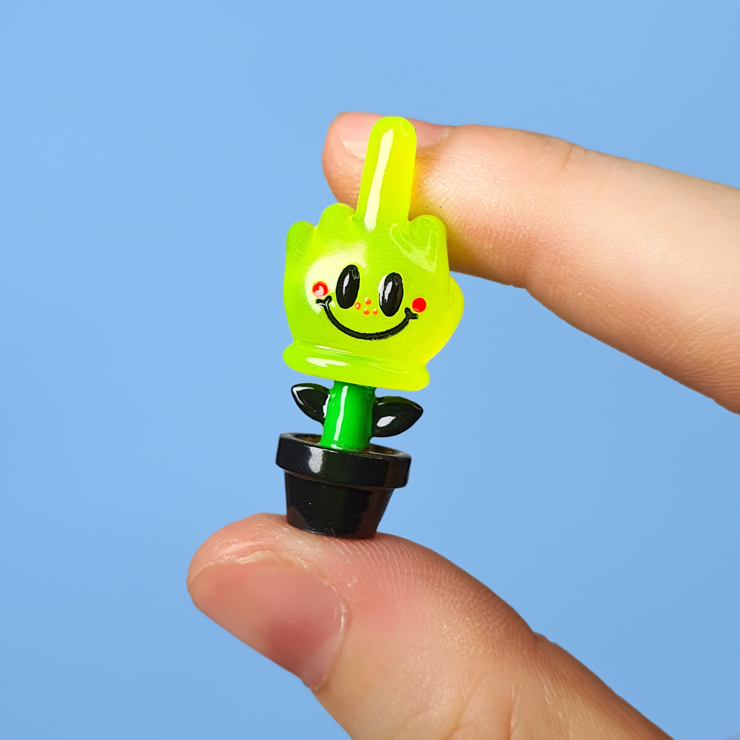 A hand holds a small green resin toy with a smiley face, part of the Little Shit Big Deal - Smile Of Hope collection by KikToyz.