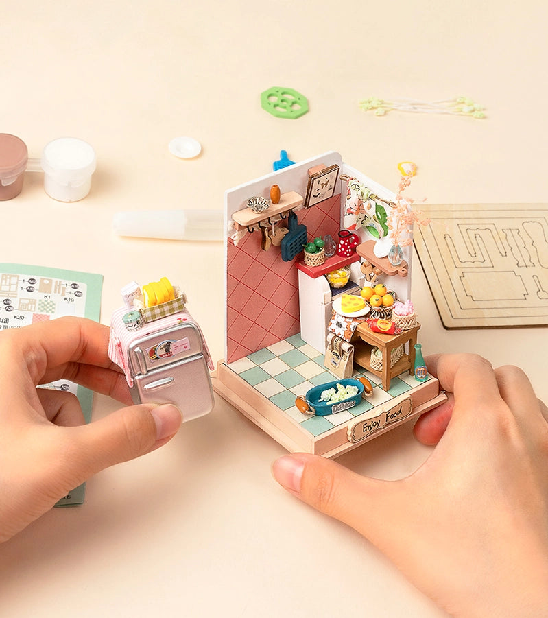 A hand holding a miniature kitchen with intricate details like spiral stairs, a cozy sofa corner, and a bookshelf. Product title: Taste Life - Kitchen Mini Diy House. From Strangecat Toys, a blind box and art toy store.