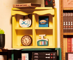 A yellow shelf with a clock, book, and sign. Book Nook Kits For Adults - Bookstore. Enhance your space with this creative DIY kit. Dimensions: 9.1 x 12.2 x 1.8 in.