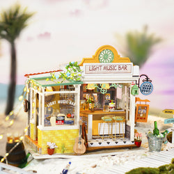 A miniature DIY wooden dollhouse resembling a light music bar on the beach, featuring a yellow chair, guitar, and mini bar setup. Reflects Strangecat Toys' blind box and art toy store essence.