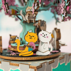 Wooden DIY Music Box Cherry Blossom Tree with cat and dog figurines on a tree, cartoon cat, and puzzle. Intricate design for a joyful, storytelling melody experience. From Strangecat Toys.