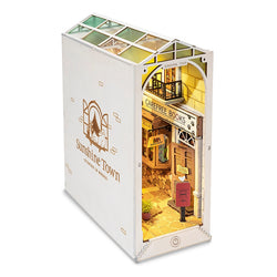 Book Nook Kits For Adults - Sunshine Town: A small white box resembling a book store with a tiny building inside, evoking Tokyo streets in spring. Dimensions: 9.1 x 12.2 x 1.8 in.