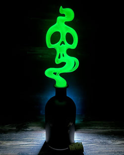 A green skull-shaped resin bottle topper with a silicone base for wine safety. Preorder: GREEN SKULL TOXIC TONIC BOTTLE TOPPER by Saint Monday Studio. Height: 7 1/4”, width: 2 3/4”.