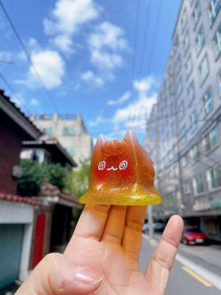 A hand holding the Too Hot! Ice Cream Cat by Rato Kim, a small orange and yellow resin toy with artificial fur.