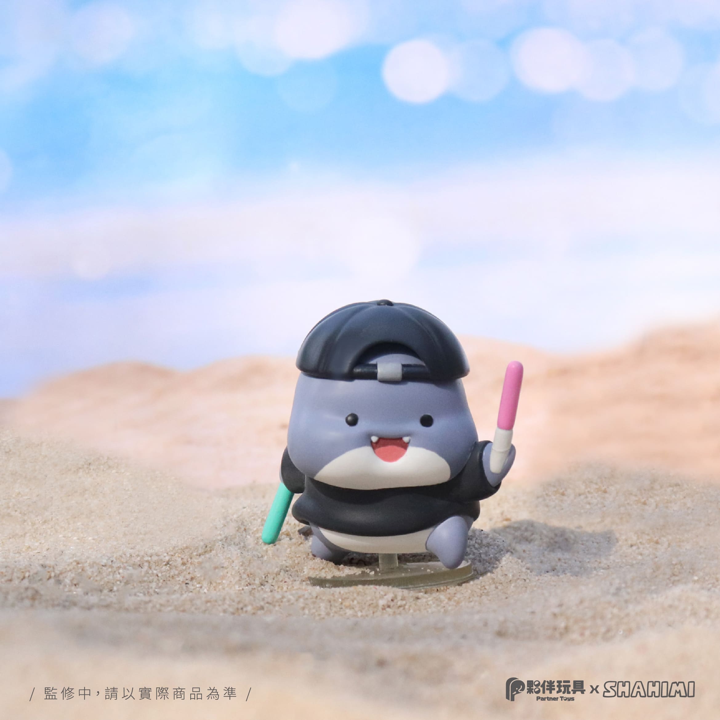 A Shahimi Shark 2 Blind Box Series toy animal on the beach, holding a stick. Preorder - Ships July 2024. Available at Strangecat Toys.