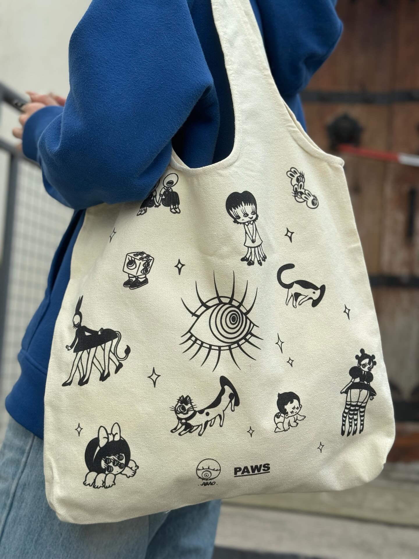 A person wearing a Momochan Tote Bag by Abao x Grape Brain, adorned with cartoon characters.