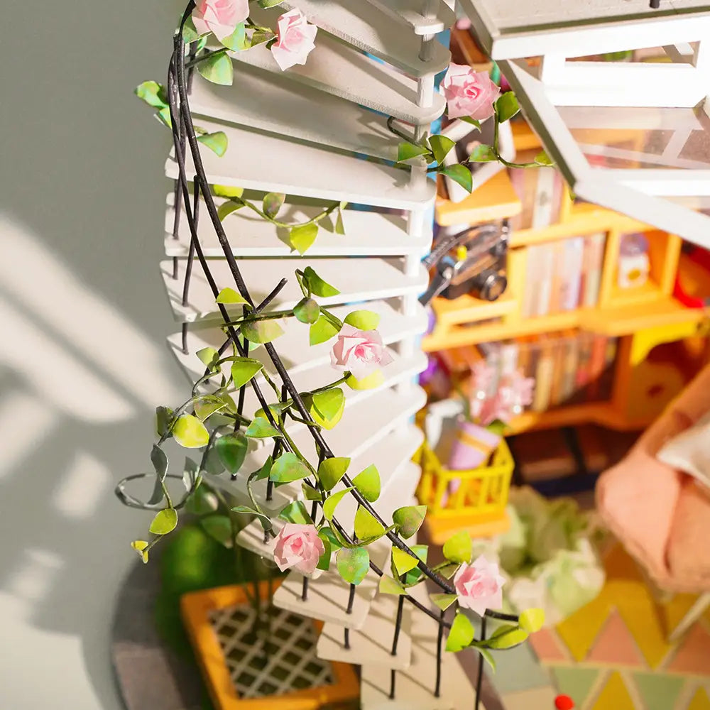 A miniature dollhouse kit named Dora's Loft Diy Miniature House with a spiral staircase adorned with pink flowers and green leaves, embodying the joy of assembling and peacefulness. Dimensions: 8.3 x 2.6 x 10.5 in.