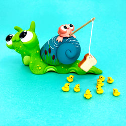 Small figurine of a snail fishing with rubber ducks and a pink frog toy, part of Simon Says Macy & Friends - Gone Fishin'.