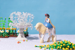 Toy figurine of a girl riding a unicorn with a crystal garland vase, bell, and flowers.