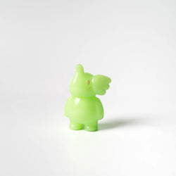 A lime green toy bird, Elfie 100% by Too Natthapong, stands on a white surface. Reflecting Strangecat Toys' blind box and art toy store ethos.