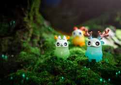 Tiny Muffinn toy set with glow-in-the-dark elements on moss, a blue toy with antlers, and a white object.