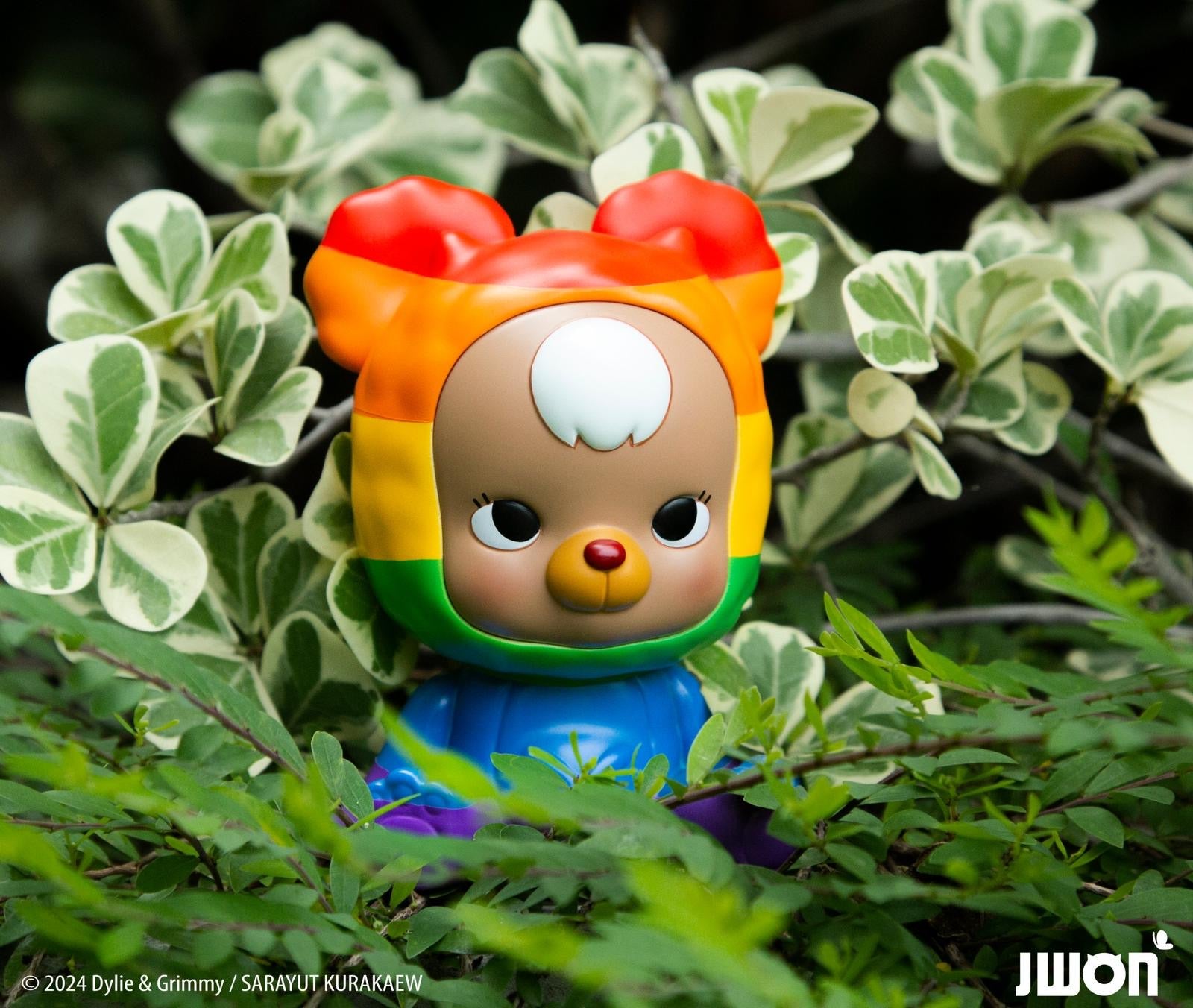 Alt text: Jrbo Rainbow Edition by JWON, a 10cm resin toy bear figurine, nestled among bushes. Preorder, ships July 2024.