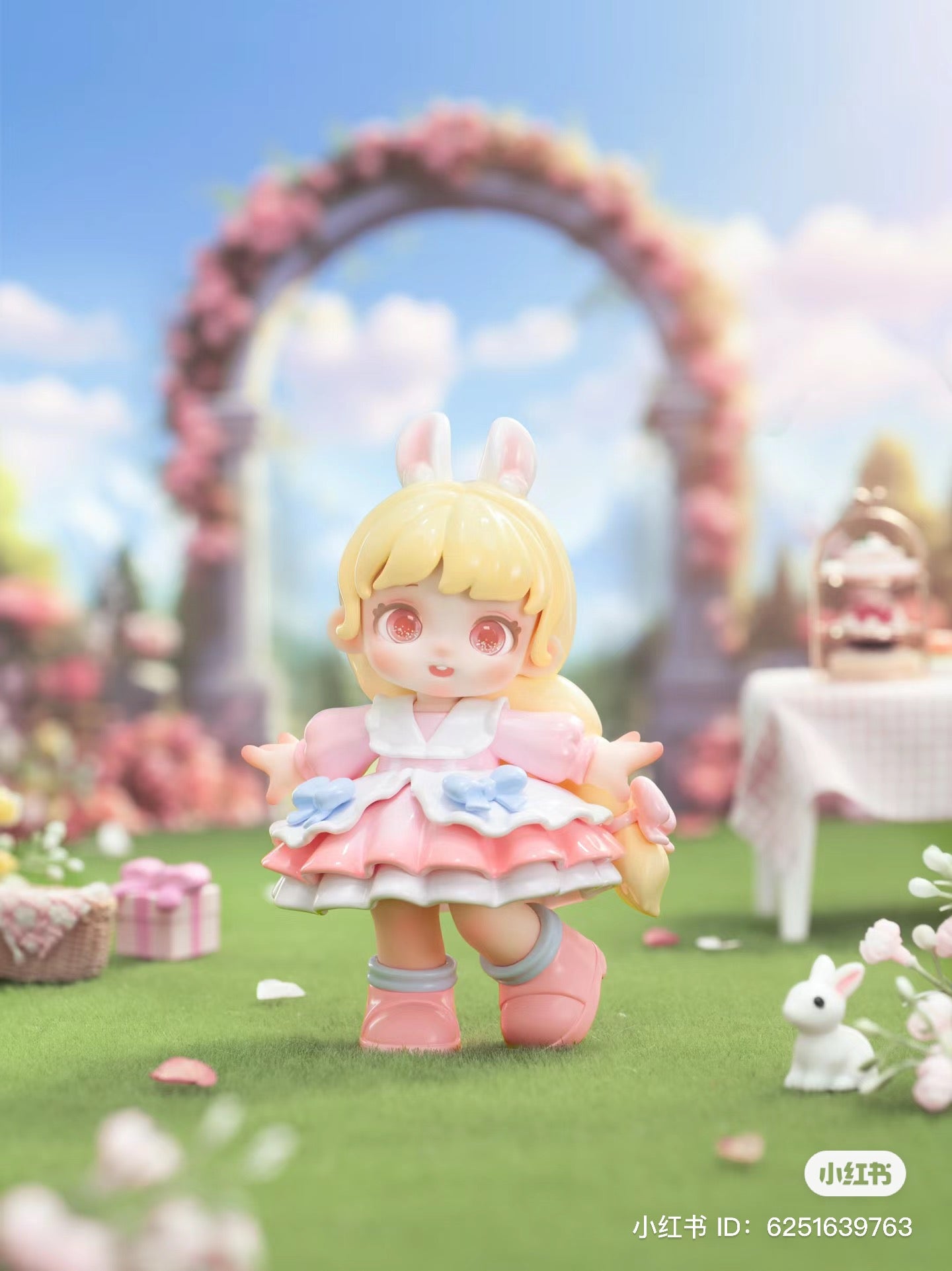 Alt text: Miana - Tea Party In The Forest Blind Box Series toy doll with bunny ears and pink dress, displayed in a garden setting.