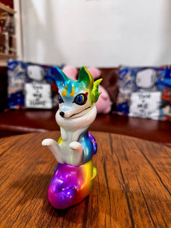 A colorful toy figurine of Urukoma - Metallic Rainbow by YASU on a wooden surface, limited edition Japanese Sofubi, 13cm, 25 pieces.