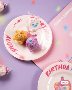 A group of small toys on a plate, including a purple skull toy and a yellow unicorn hat toy from the ShinWoo Candle Set.