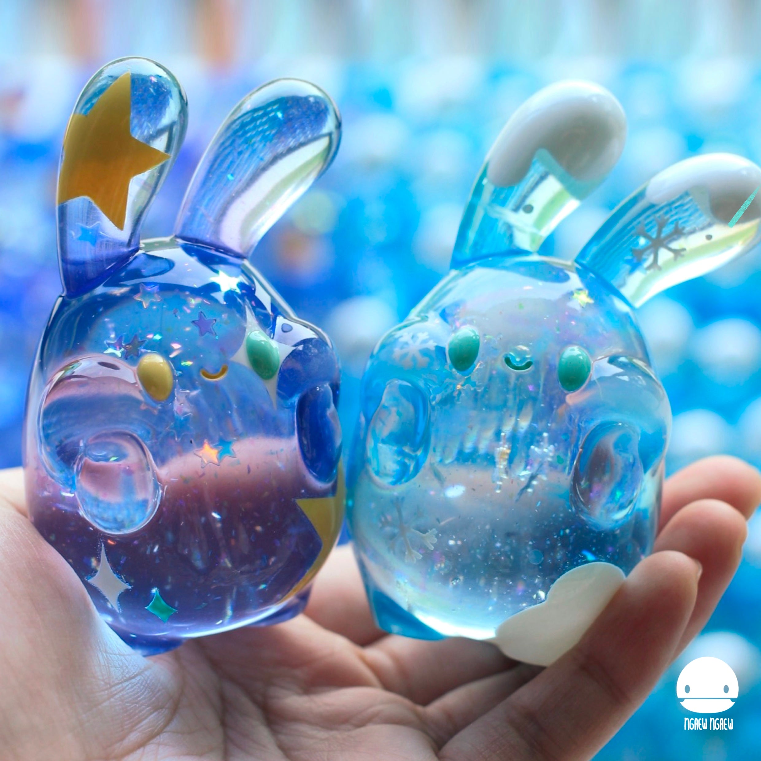 Hand holding Ngaew Ngaew Shooting Star & Falling Snow resin figurines, 8cm in height, showcasing blue and white bunny characters with star motifs.