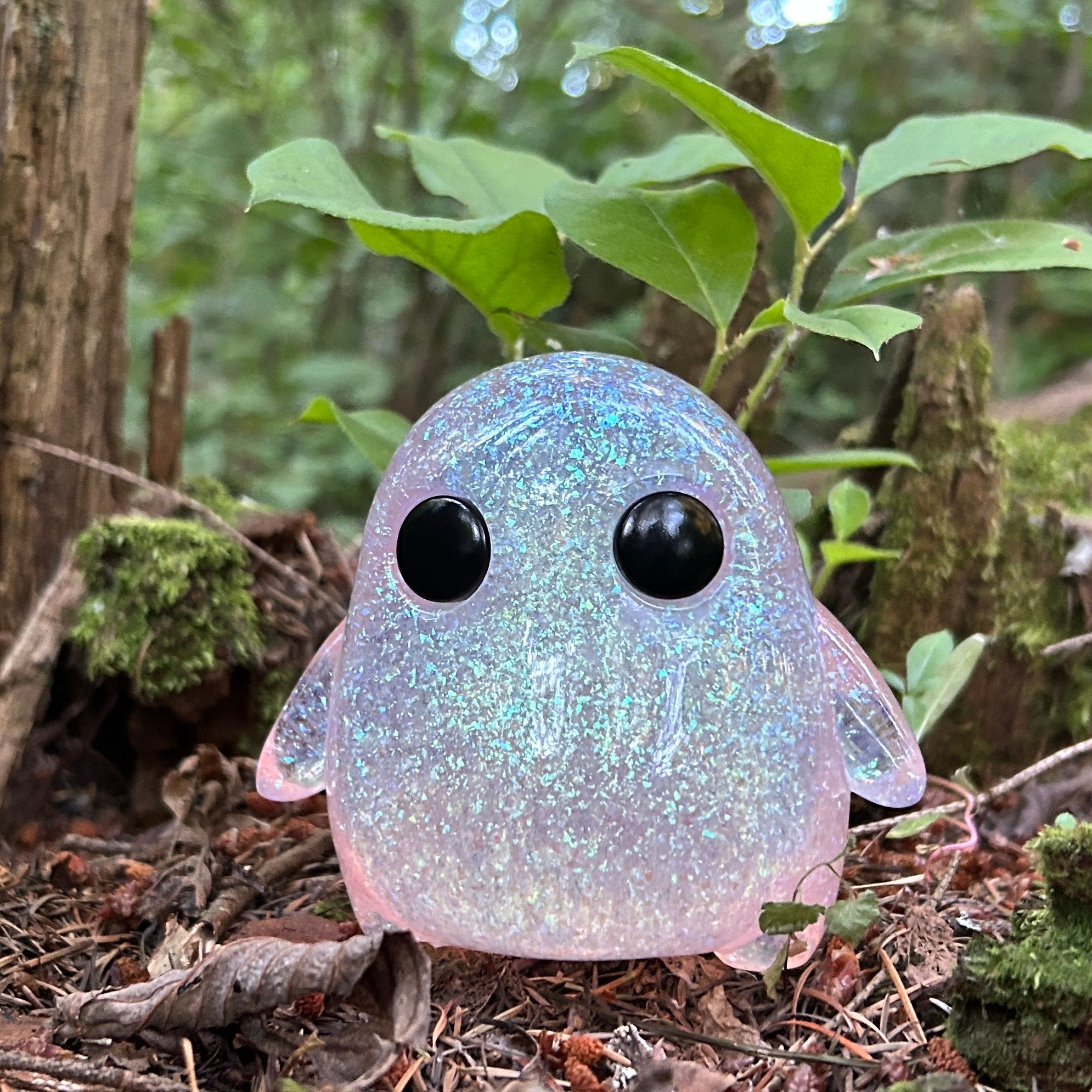 Galaxy Stubby by The Lostlings, a 10cm resin toy with black eyes and a pink body, displayed outdoors among trees. Limited edition of 50 pieces.