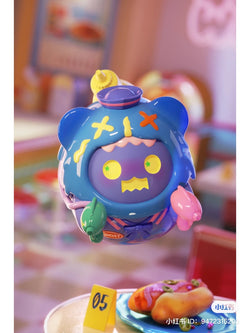 A toy from the ShinWoo Ghost Diner Blind Box Series, featuring various designs including a blue toy with yellow eyes and a hat, a green balloon, and a yellow object with a green star.