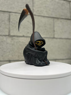 A toy figure of a Grim Reaper holding a scythe, with a gold skull detail, limited edition by Riser, 9 tall.