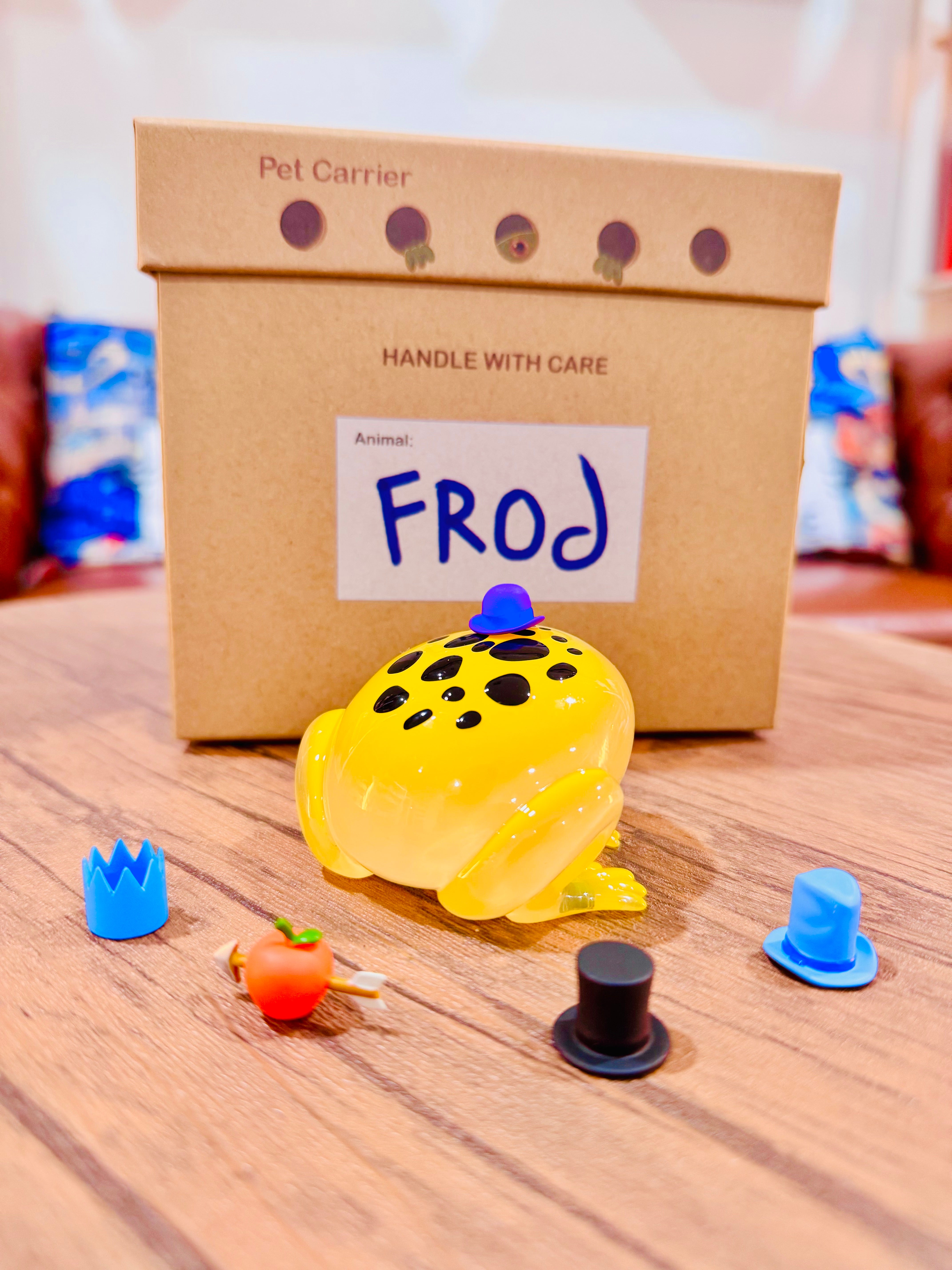 Poison Dart Frod by Sad Salesman, a 9cm resin frog toy with five interchangeable PVC hats, displayed next to its packaging. Limited edition of 100 pieces.