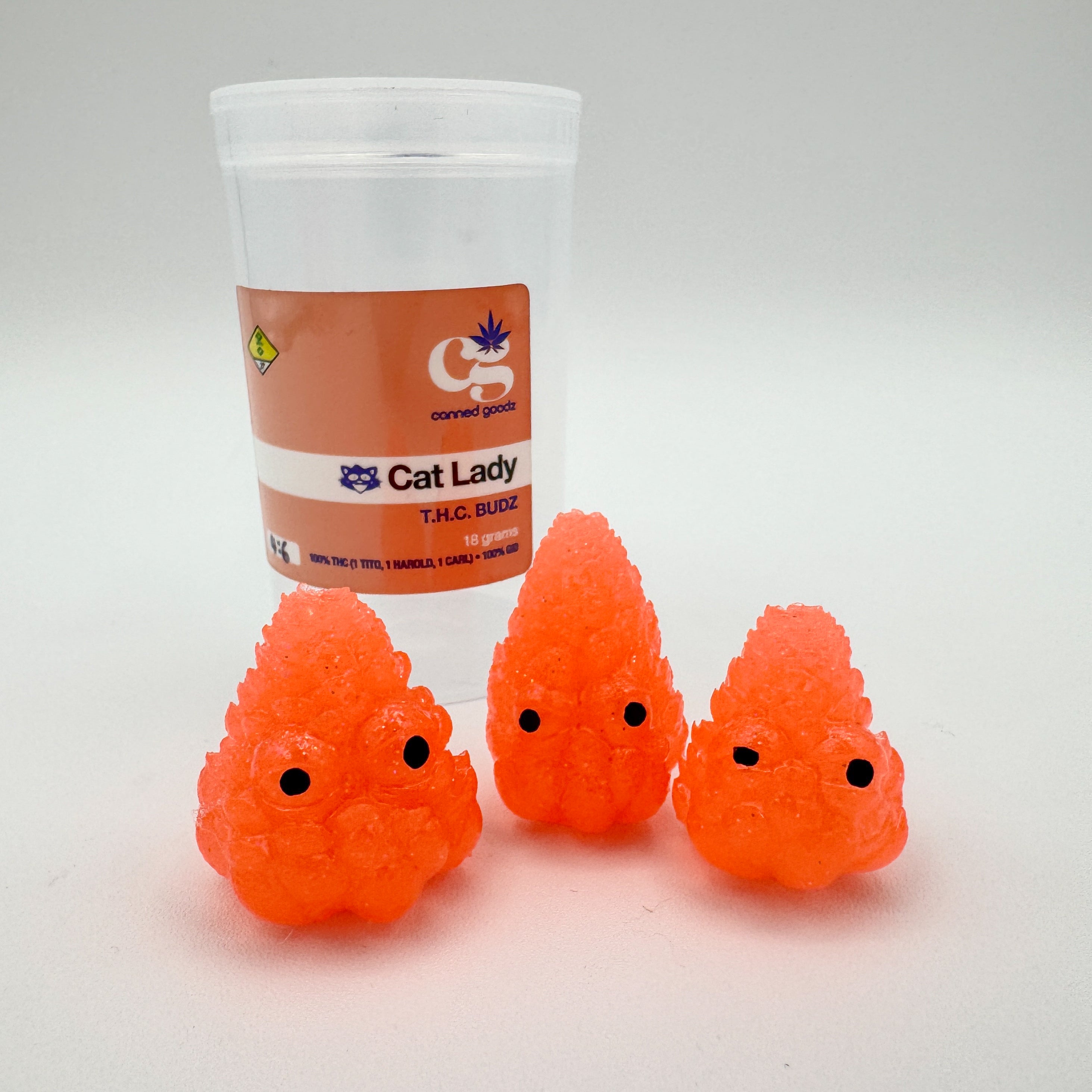 Hello World - THC BUDZ by JFO, featuring a group of orange toy objects with black eyes, next to a plastic container.