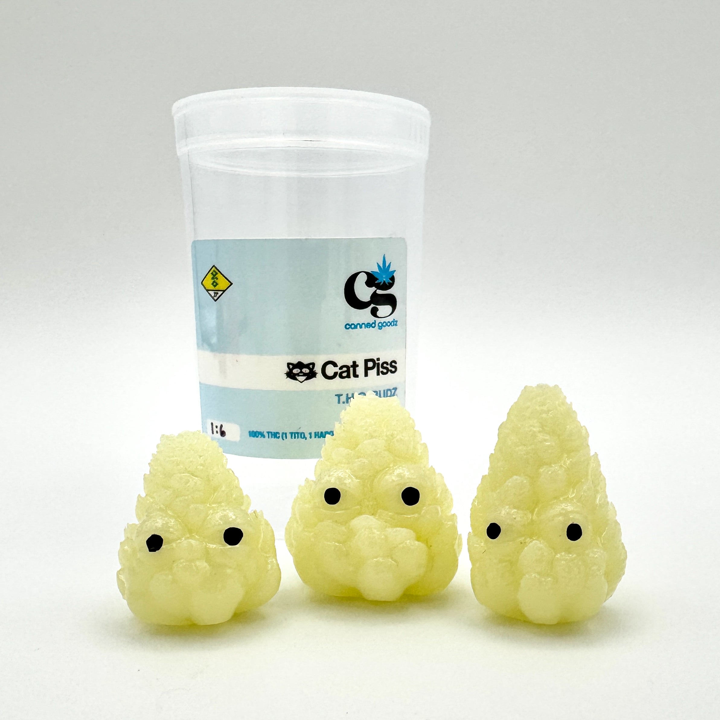 Hello World - THC BUDZ by JFO, a set of three yellow plush toys with black eyes, displayed next to a labeled plastic container.