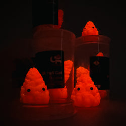 Hello World - THC BUDZ by JFO, featuring a set of three orange and red toy figures with distinctive facial features, showcased in a dark setting.