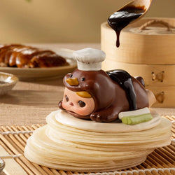 A small toy atop pancakes, chocolate duck with chef hat, cake close-up, wooden spoon with liquid, chef's hat - PUCKY The Feast Blind Box Series - Preorder.