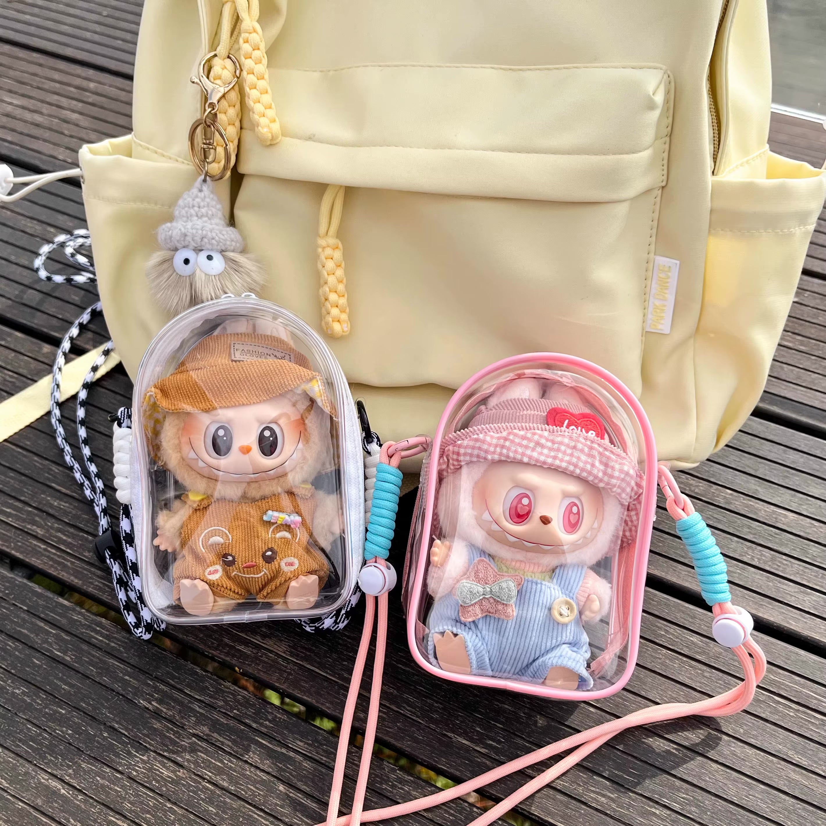 Protect Case 15cm Cotton Doll Shoulder Bag featuring two stuffed toys in clear cases next to a backpack, perfect for toy enthusiasts.