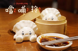 Dumpling baby by Kiwi figurine next to a bowl of food and soup with chopsticks.