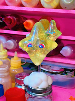 Resin toy of a star-shaped figure with eyes on a stick, part of the Bling Baby Yellow collection by Kiwi.