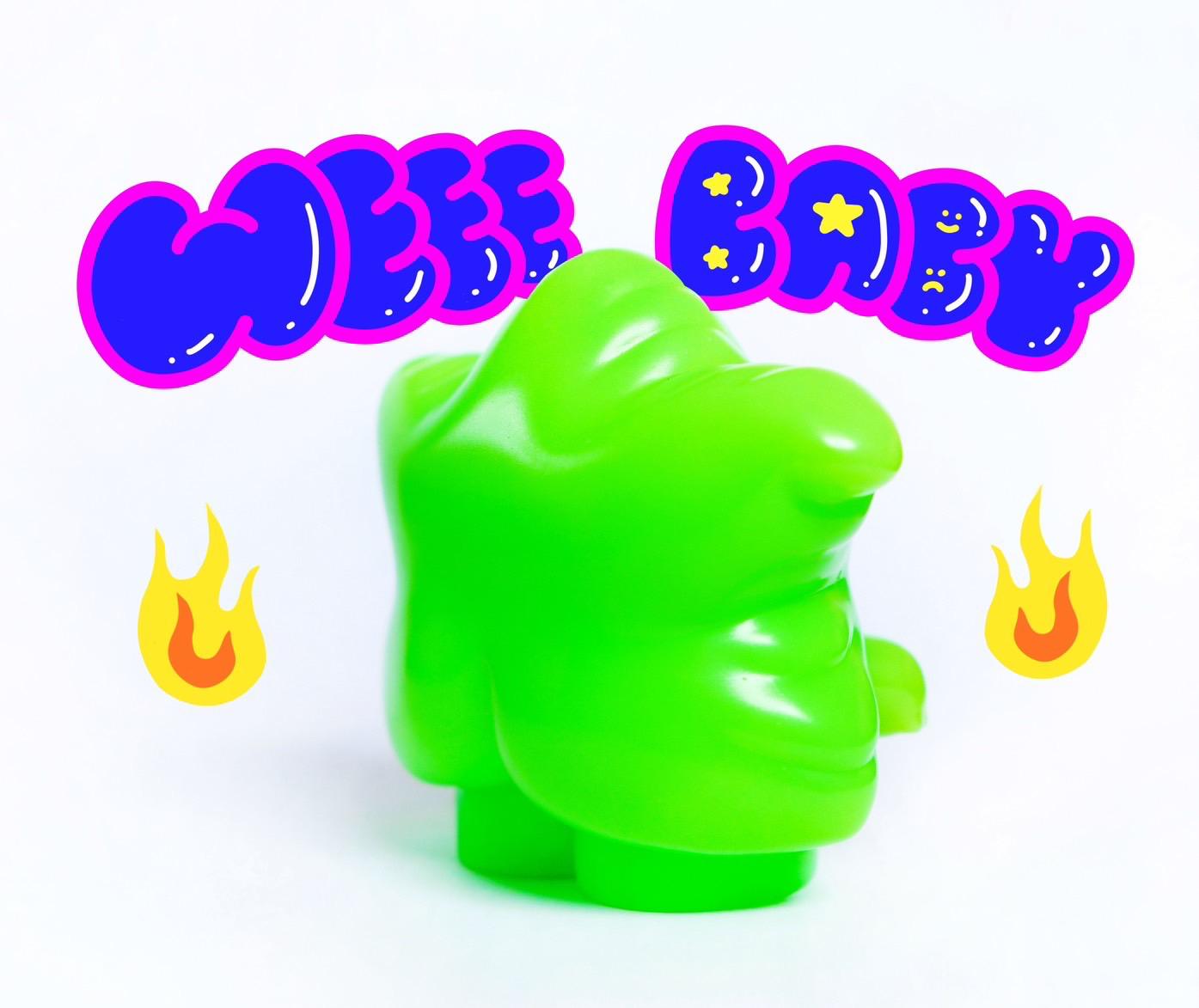 Cartoon toy with text overlay, green plastic object with blue and pink letters, yellow and orange flame.