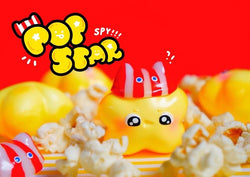 A yellow toy star with a striped hat and popcorn, part of the Popstar collection from Strangecat Toys.