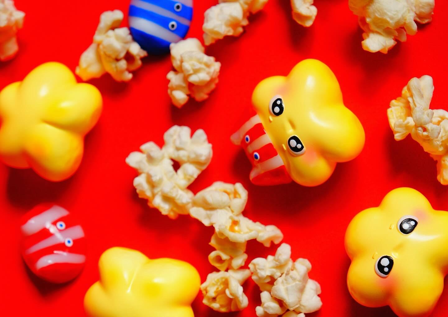 Popcorn, toys, and a yellow bell pepper on a red surface, with a close-up of a blue striped toy and a yellow object, part of the Popstar collection.