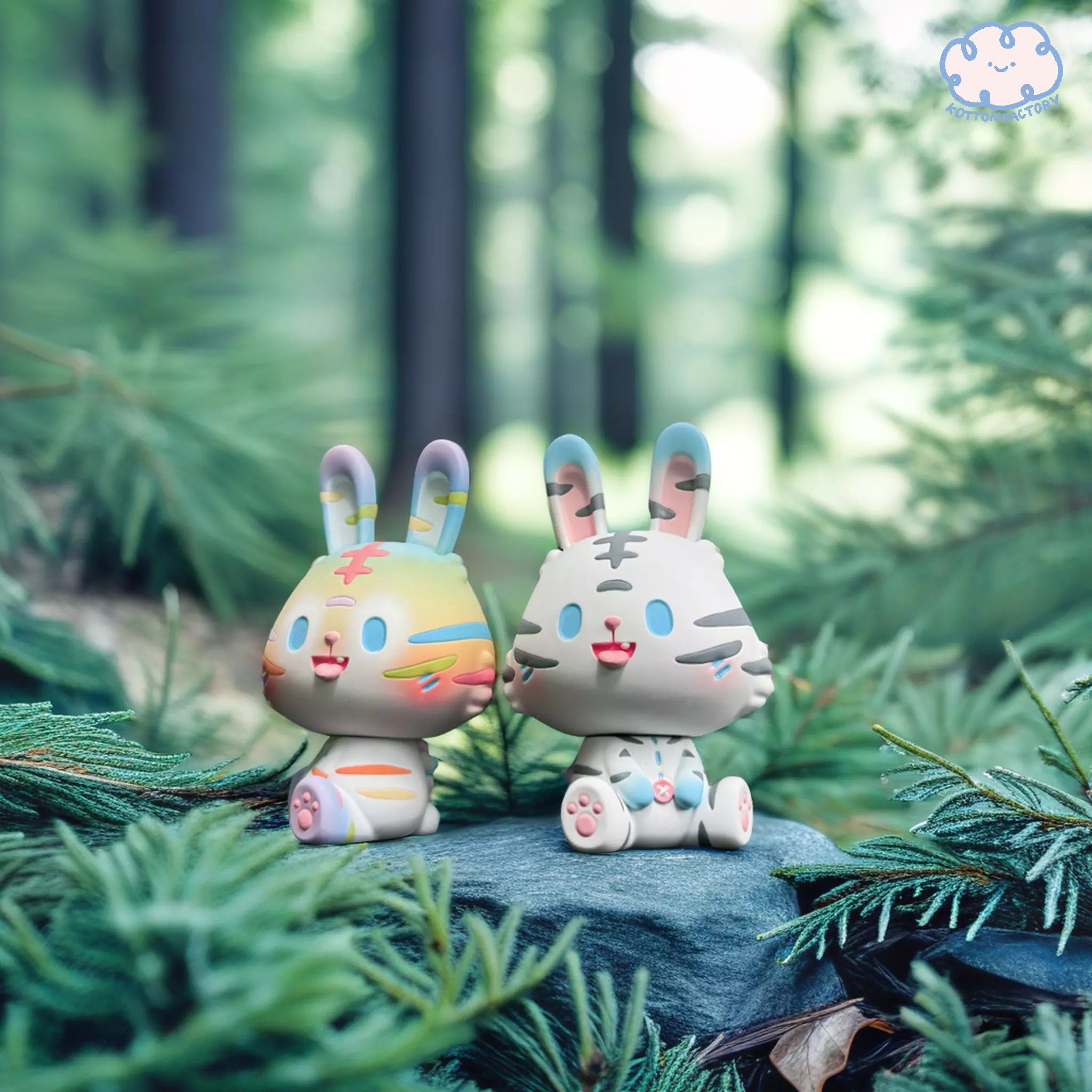 Two small resin toys, Tiger - White & Rainbow Robin by Kotton Factory, displayed outdoors on a rock, limited edition of 100 pieces.