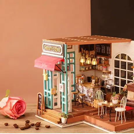 A miniature coffee shop with a pink rose, wooden furniture, lamps, and coffee beans. Simon's Coffee Diy Mini House Cafe Shop includes LED light, assembly tools, and detailed instructions. Dimensions: 12.6 x 8.1 x 2 in.