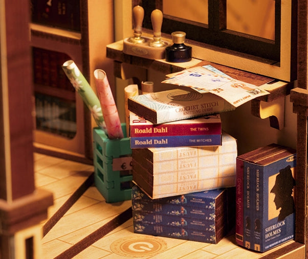 A stack of book nook kits for adults resembling a miniature bookstore scene. Includes detailed instructions, batteries required. Dimensions: 9.1 x 12.2 x 1.8 in. From Strangecat Toys.