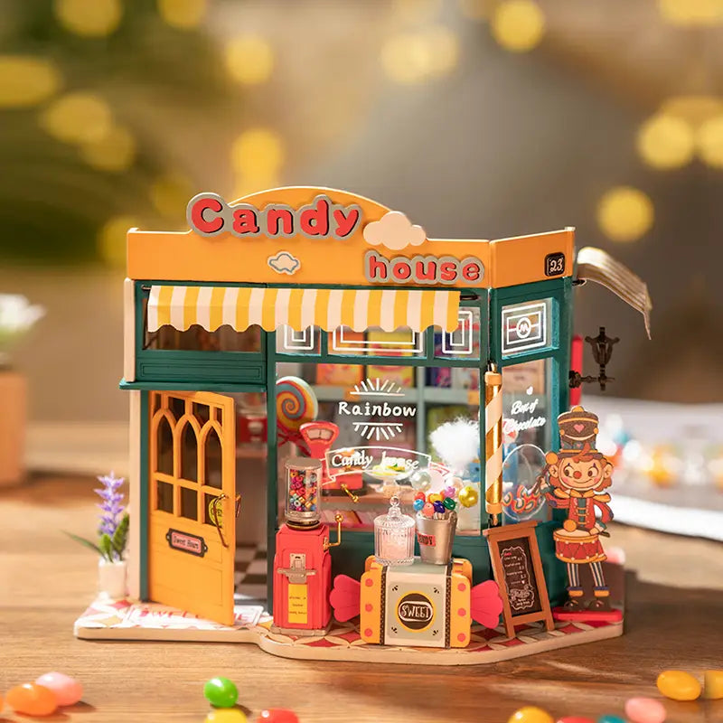 A whimsical Rainbow Candy House DIY miniature house from Strangecat Toys, featuring a magical tea time scene with a bunny, snacks, and a mystical door. Dimensions: 8.3 x 5.2 x 6.9 in.