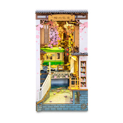 A Book Nook Kit featuring a Sakura Tram design, ideal for adults, displayed in a creative setting with a green train and a toy train model. Dimensions: 9.4 x 3.9 x 7.4 in.