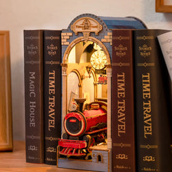 A DIY miniature house book nook featuring a train in a bookshelf, clock, and books. Book Nook Kits For Adults - Time Travel from Strangecat Toys. Dimensions: 9.1 x 12.2 x 1.8 in.