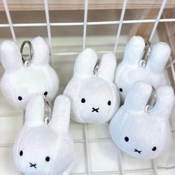 A Miffy Plush Keychain, handmade in the Netherlands, featuring a white stuffed animal with black eyes and a keychain attachment. Group of toy snowman keychains.