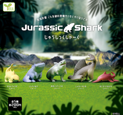 Jurassic Shark Gacha figures on grass, including a shark statue, toy shark, and toy dinosaur in a line.