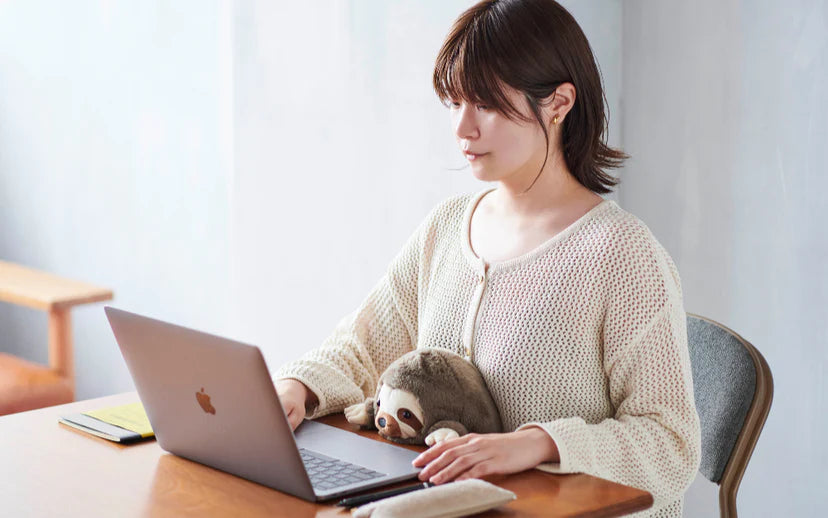 A woman uses a laptop with a Posture Pal stuffed animal on her desk to promote good posture.