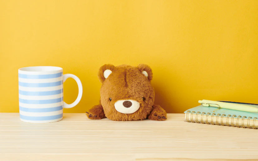 Posture Pal teddy bear sits next to a mug and notebook, designed to promote good posture while adding a cute, comforting presence to your workspace.