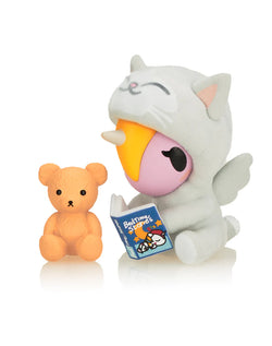 Cozy Unicorno Blind Box collectible featuring a stuffed animal in pajamas reading a book, showcasing the cozy self-care theme of this art toy series.