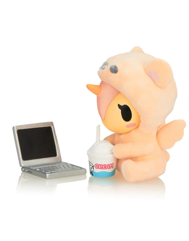 Cozy Unicorno Blind Box collectible featuring a stuffed animal with an accessory next to a small laptop, highlighting the cozy theme and art toy nature.