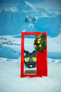 Toy in snow with wreath on red door, mountain in distance.