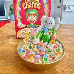 A bowl of cereal with toy figurine and box, a white toy with an x on it, indoor toy baby toys candy cartoon.