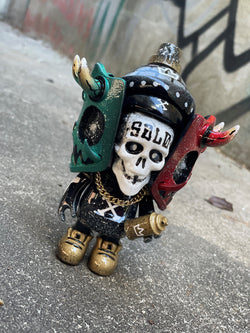 Toy figure with skull, armor, and horns, close-up of device and bottle, skull with text, statue with gold chain, red and black object, metal object, number on surface.