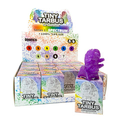 Tiny Tarbus Spectrum Blind Box Series featuring colorful boxes with various toy figurines and a stack of books with a purple dinosaur toy.